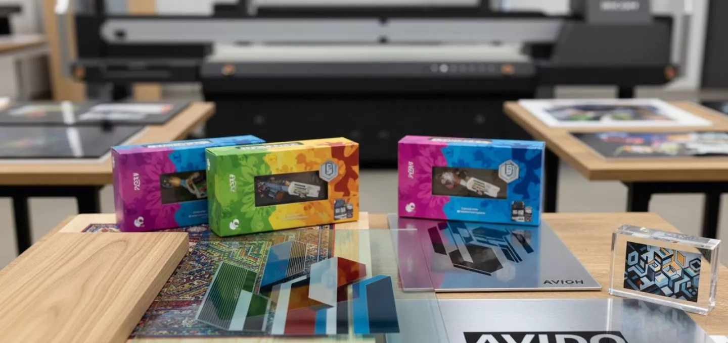 A sleek product showcase of the RICOH Pro T7210 flatbed printer in action, printing vivid, high-resolution designs onto multiple rigid substrates. The scene features a variety of materials—wood panels, glass sheets, metal plates, and acrylic boards—arranged neatly around the printer, emphasizing its media versatility. One print sample shows a vibrant interior décor design on wood, another a stylish graphic on glass, and another a bold promotional design on metal. The workspace is professional, well-lit, and creative, highlighting the printer’s ability to handle substrates up to 110 mm thick. The overall composition conveys innovation, flexibility, and opportunity for expanding into markets like décor, packaging, and promotional products.